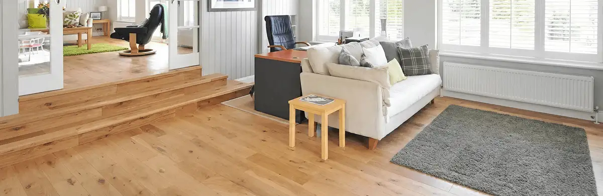 A modern living room with professionally installed laminate flooring, a beige sofa, a small side table, a gray rug, and large windows with white shutters in Sioux Falls, SD